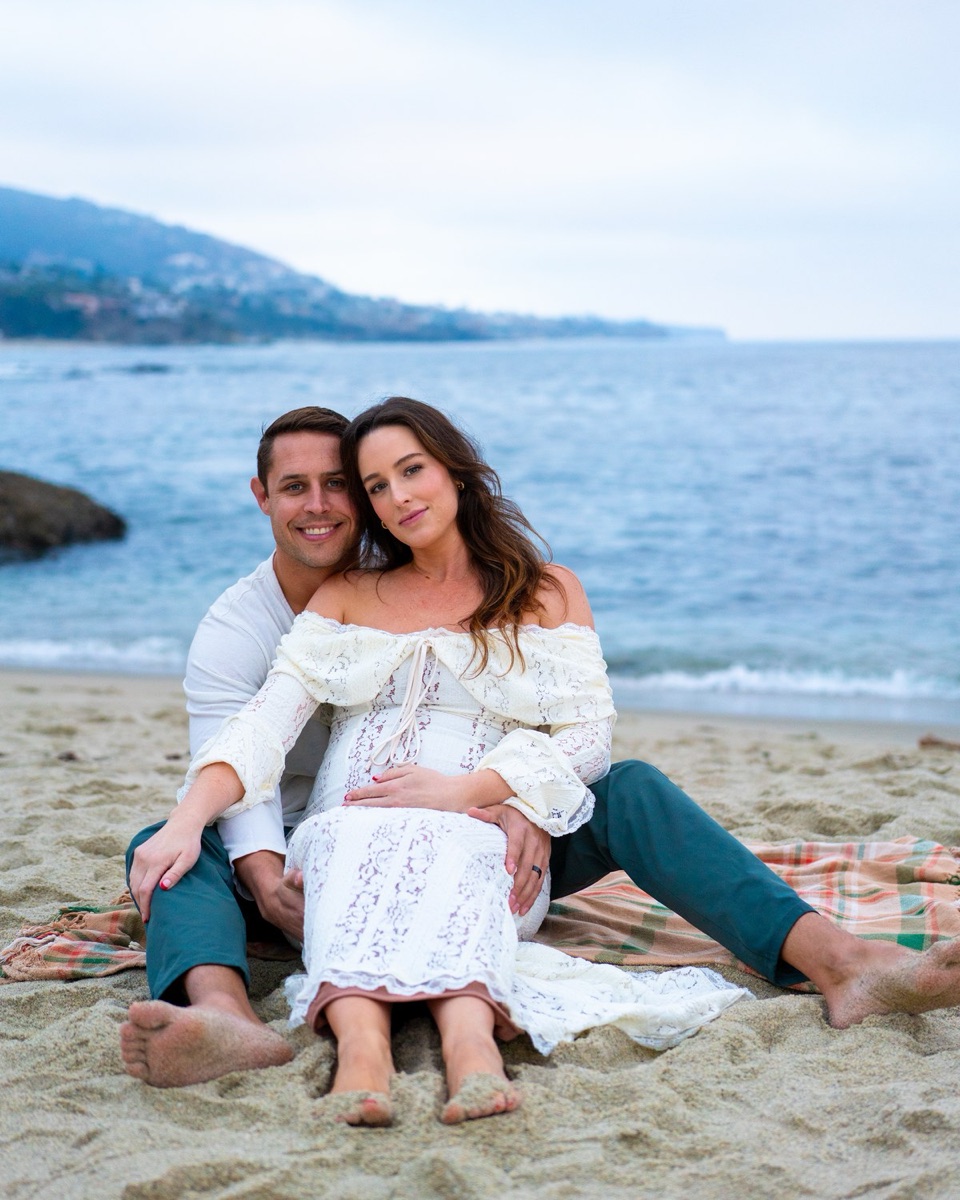 Pregnant woman reclined against her partner on the sand, fully supported, eyes closed