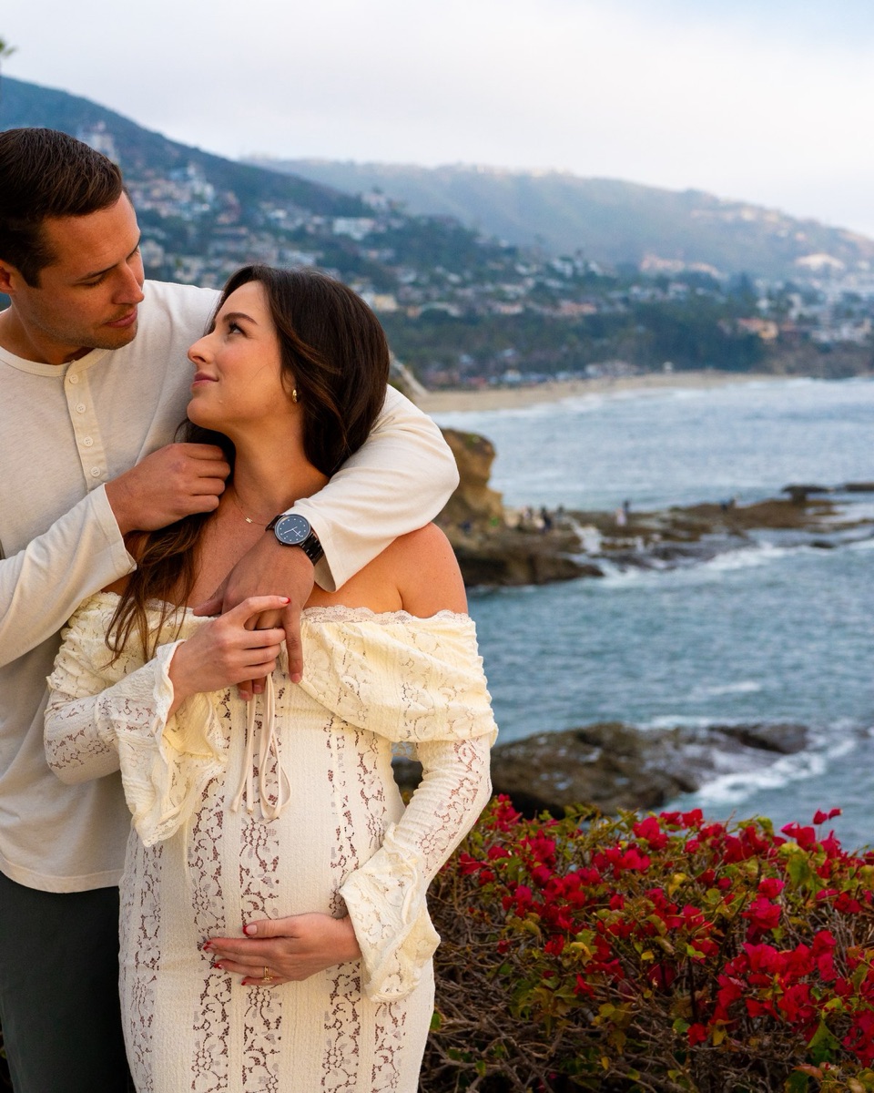 Pregnant woman leaning back into her partner's chest on the beach at blue hour, looking up at him