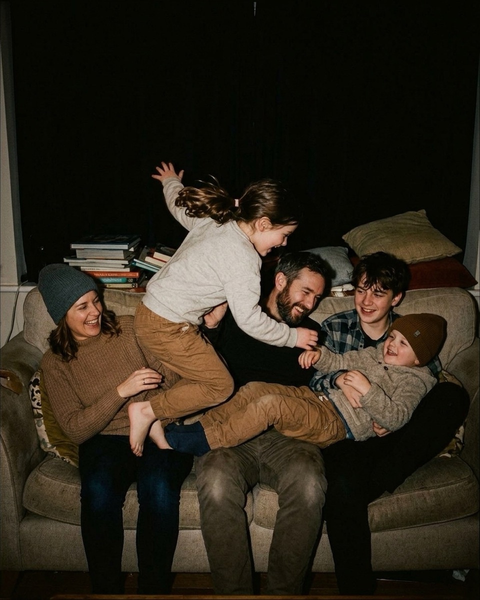 Family piled together laughing on a couch at night, lit with flash