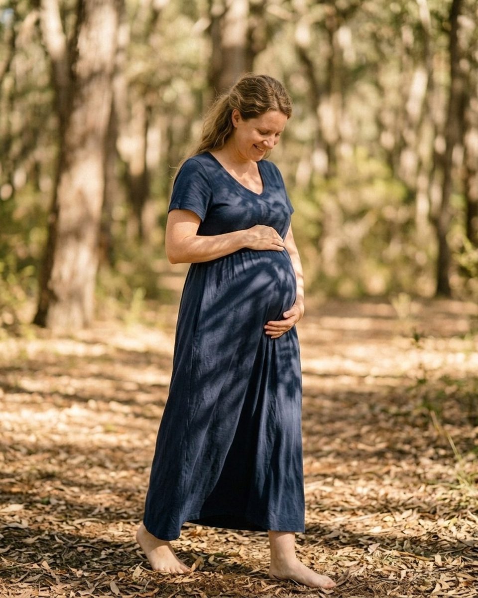 Pregnant woman standing barefoot at a garden edge in soft overcast light