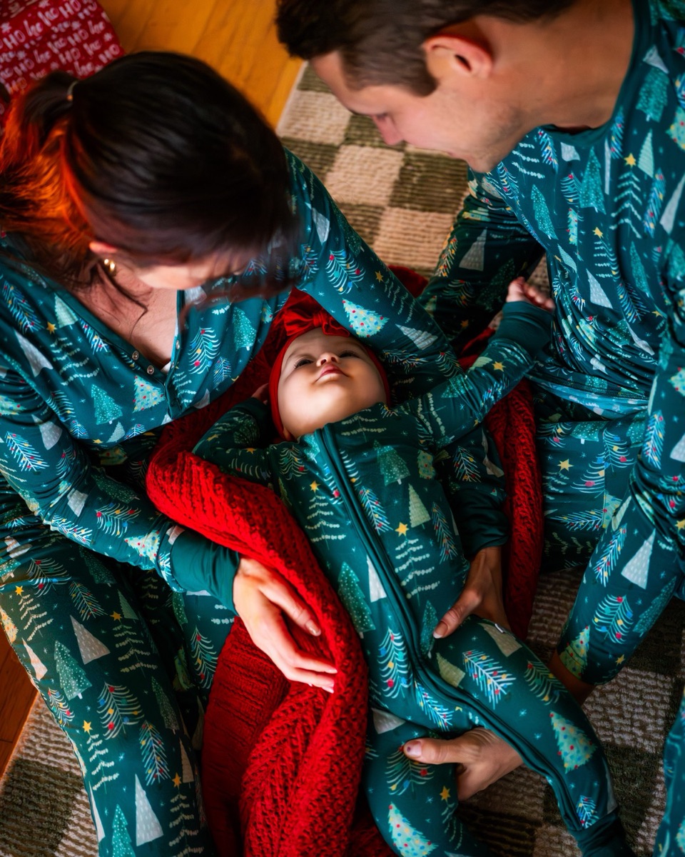 Two parents cradling baby between them on a red blanket, shot from overhead