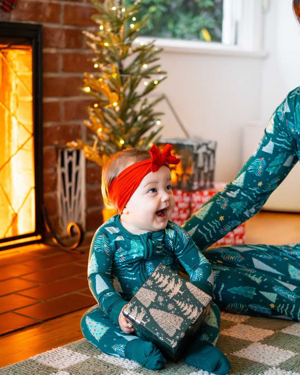 Mother watching her baby hold a small wrapped gift on a rug by the fireplace
